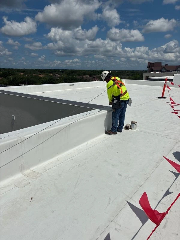 Roofing crew member applying a white flat roof coating system on a commercial building rooftop